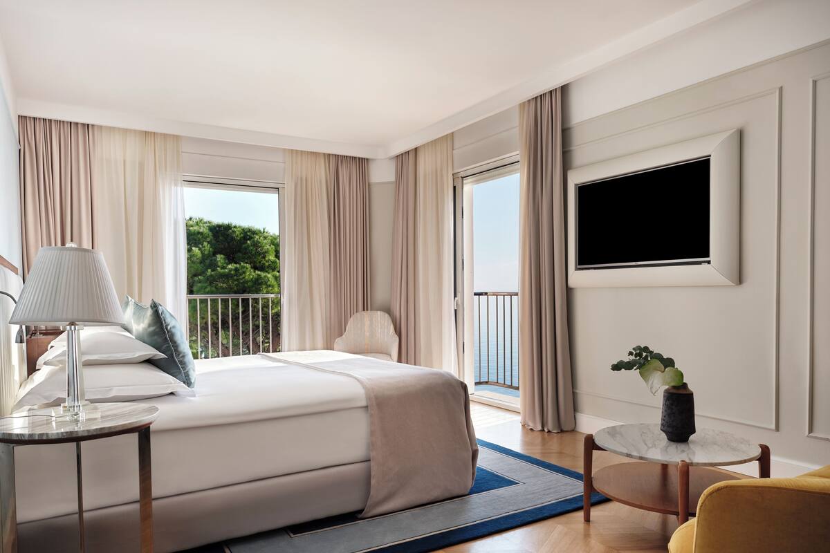Habitación de hotel con cama, televisión, una mesita, una silla y vistas al exterior.