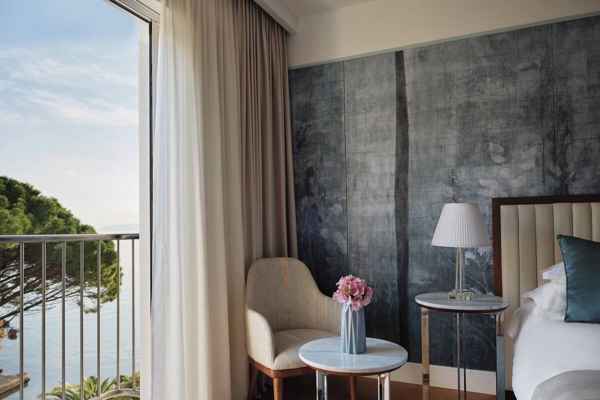 Habitación de hotel con cama, una silla, una mesita y vistas a un cuerpo de agua.