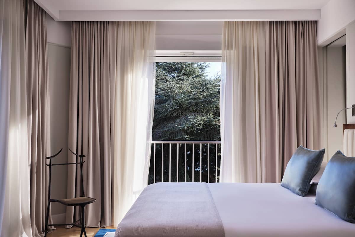 Un dormitorio con una cama grande, vistas a árboles por la ventana y una silla junto a la ventana.