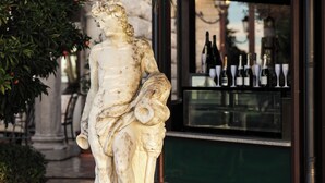Una estatua de una mujer sosteniendo una lira, ubicada frente a un bar con botellas y copas de vino.
