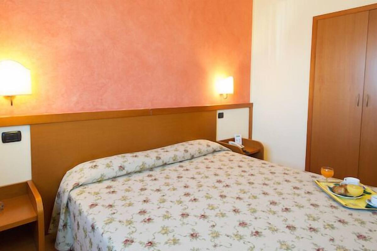 A hotel room with a bed, a bedside table, a tray with breakfast items, and a wardrobe.
