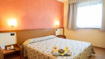 Une chambre d’hôtel avec un lit, une table de chevet, une commode et une fenêtre avec des rideaux.