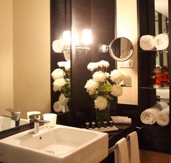 A bathroom with a large mirror, a sink, and a vase with white flowers.
