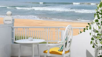 A balcony with a white table and chair, overlooking a beach with waves.