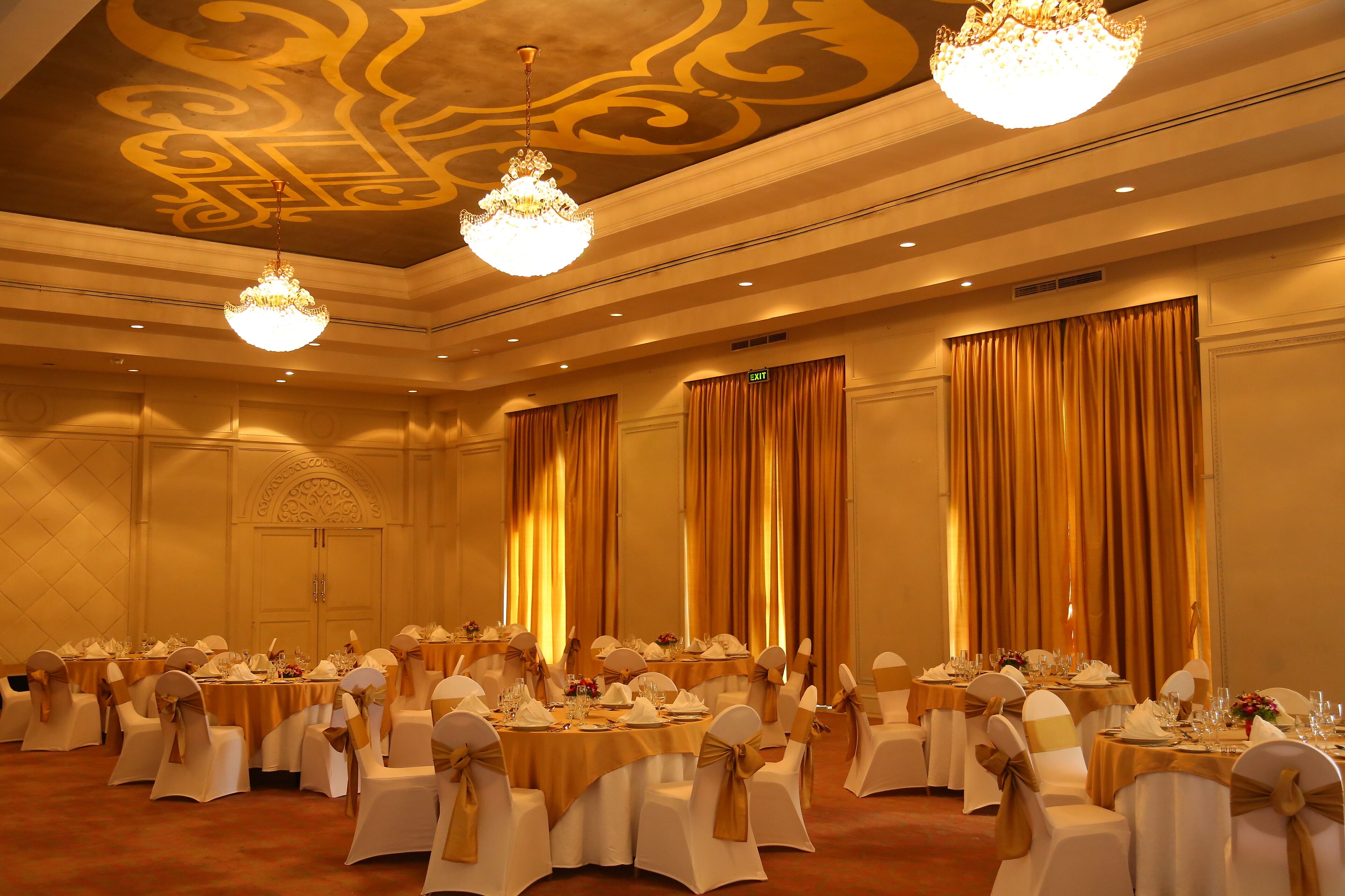 Une salle de banquet avec des tables rondes, des chaises blanches ornées de rubans dorés et des lustres.