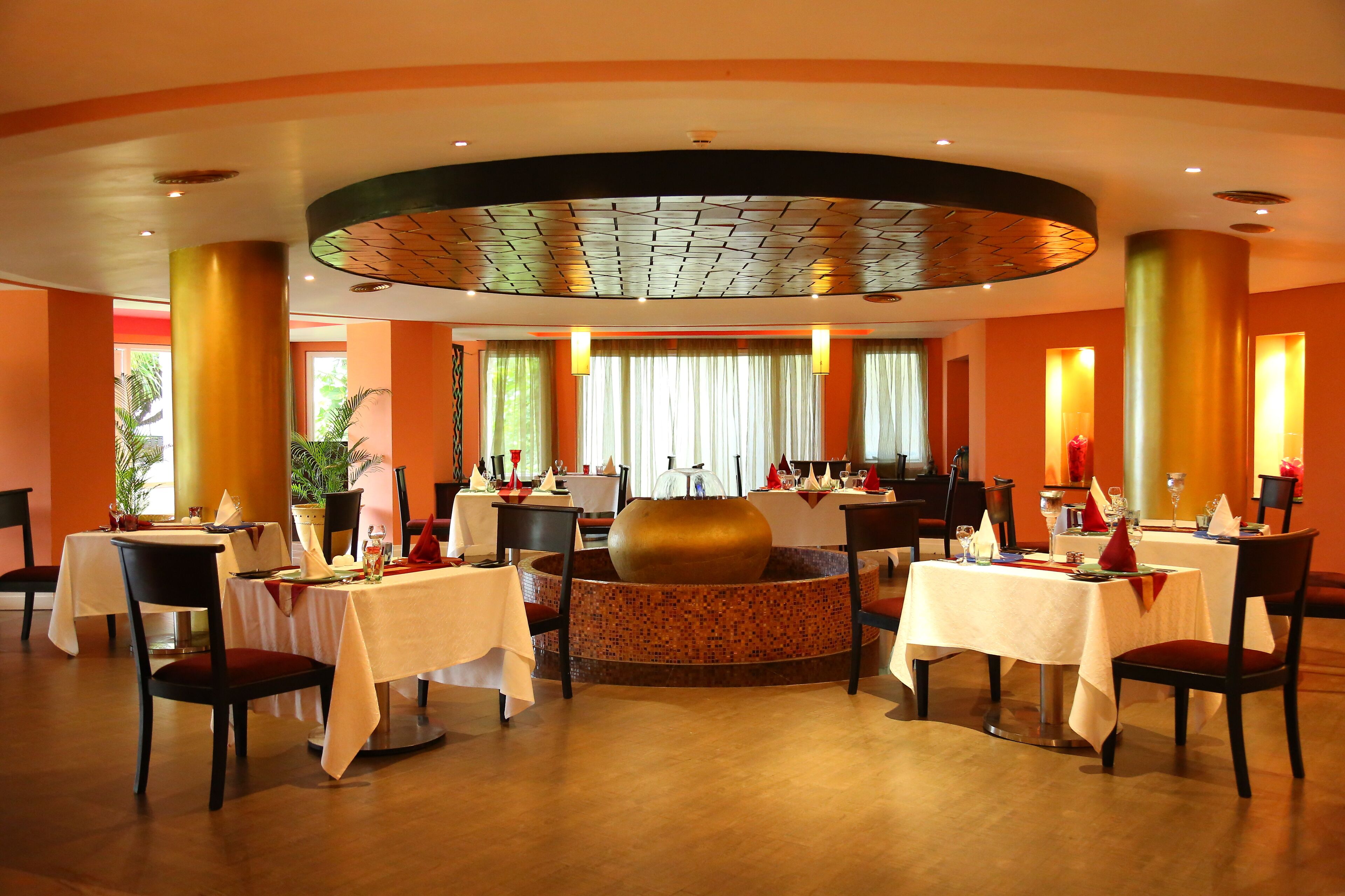 Un restaurante con mesas redondas, sillas y un elemento decorativo central.