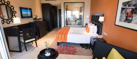 A hotel room with a bed, a desk, a chair, a sofa, a mirror, a TV, and a window.