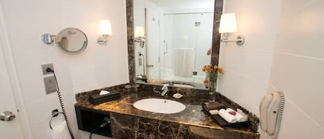 A bathroom with a marble countertop, a sink, a mirror, a towel rack, a telephone, and a vase with flowers.