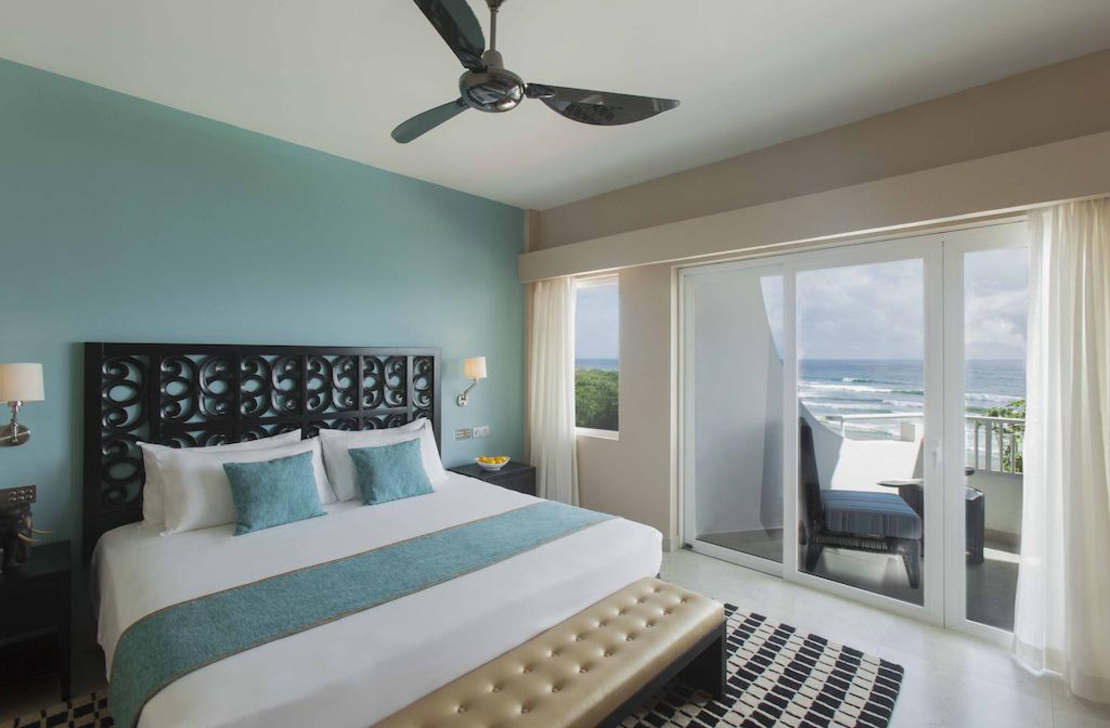Ein Schlafzimmer mit einem großen Bett, einem Deckenventilator, Meerblick durch eine Schiebetür und einem Balkon mit einem Stuhl.
