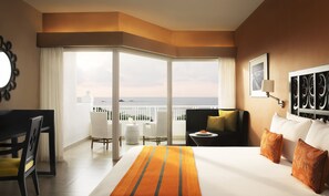 A hotel room with a large bed, a desk, a chair, and a view of the sea. - Taj Bentota Resort & Spa (Bentota)