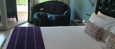 A hotel room with a large bed, a chair with a table, a window with curtains, and a wall-mounted speaker.
