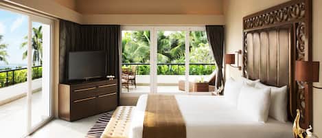 A hotel room with a large bed, a television, a ceiling fan, a balcony with a view of palm trees, and a large window.
