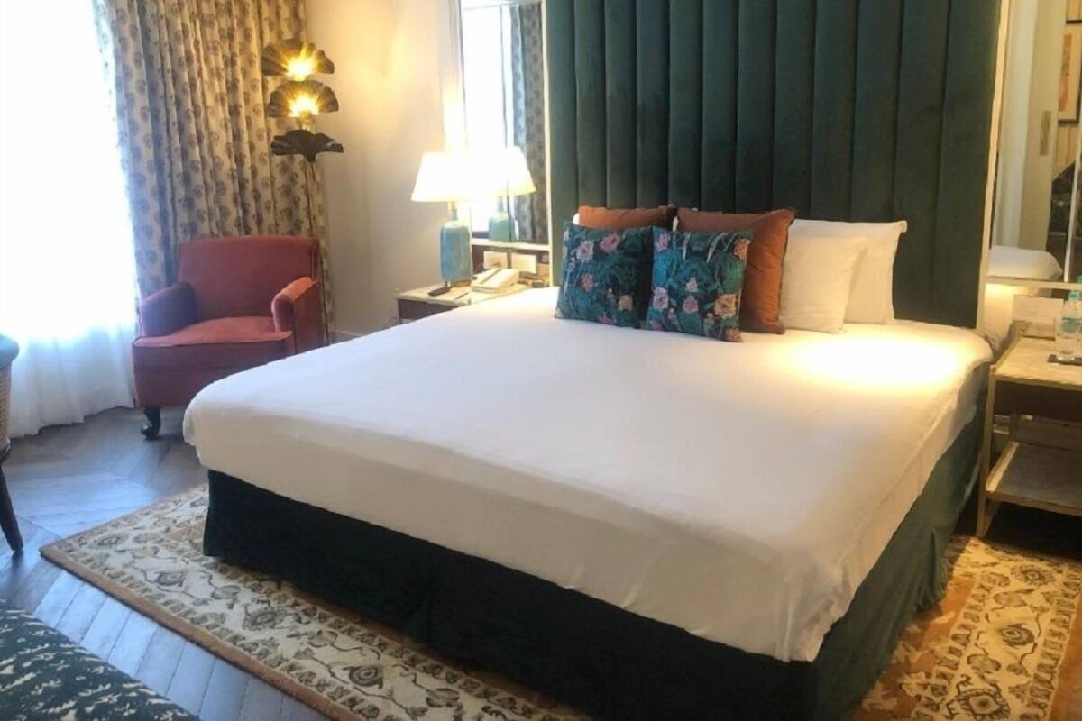 A hotel room with a large bed, a chair, a desk with a lamp, and a window with curtains.