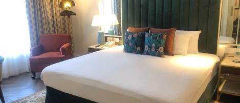 Una habitación de hotel con una cama grande, una silla, un escritorio con lámpara y una ventana con cortinas.