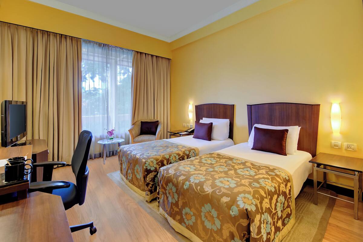 A hotel room with two beds, a desk, a chair, a TV, and a small table.