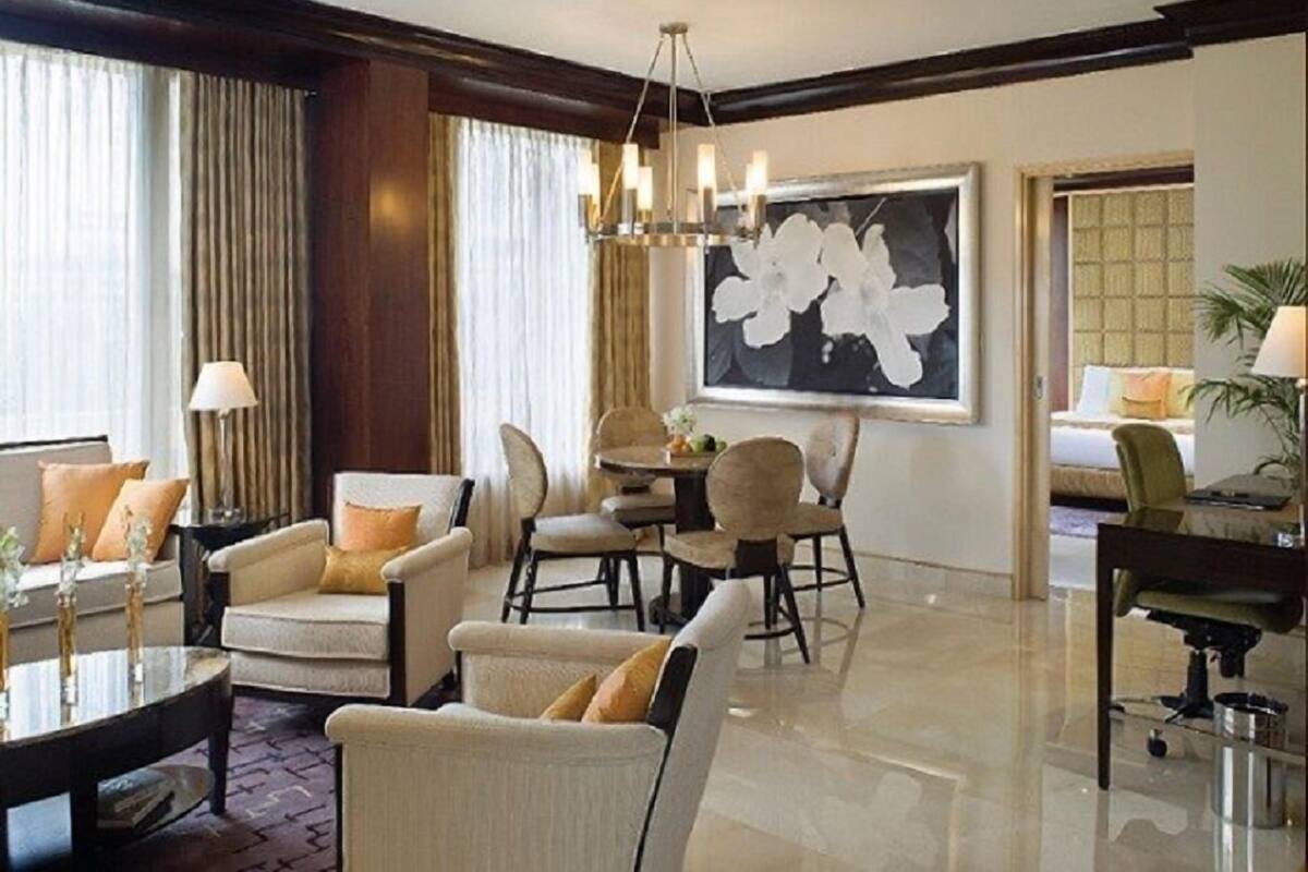 A spacious living room with a chandelier, comfortable seating, and a large floral artwork on the wall.