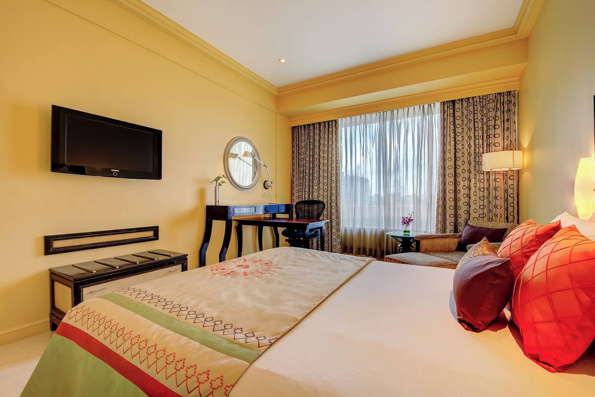 A hotel room with a bed, a desk, a chair, a TV, a lamp, and curtains.
