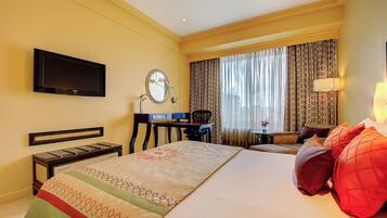 A hotel room with a bed, a desk, a chair, a TV, a lamp, and curtains.