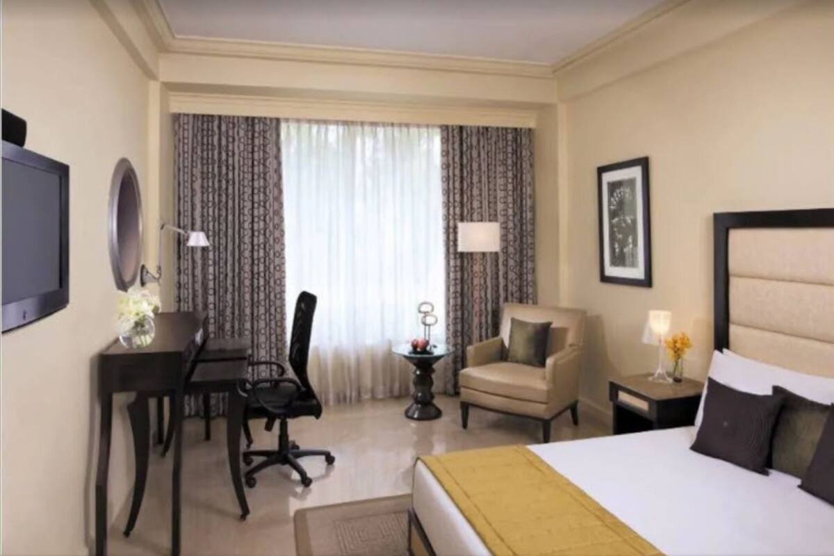 A hotel room with a bed, a desk, a chair, a small table, and a TV.