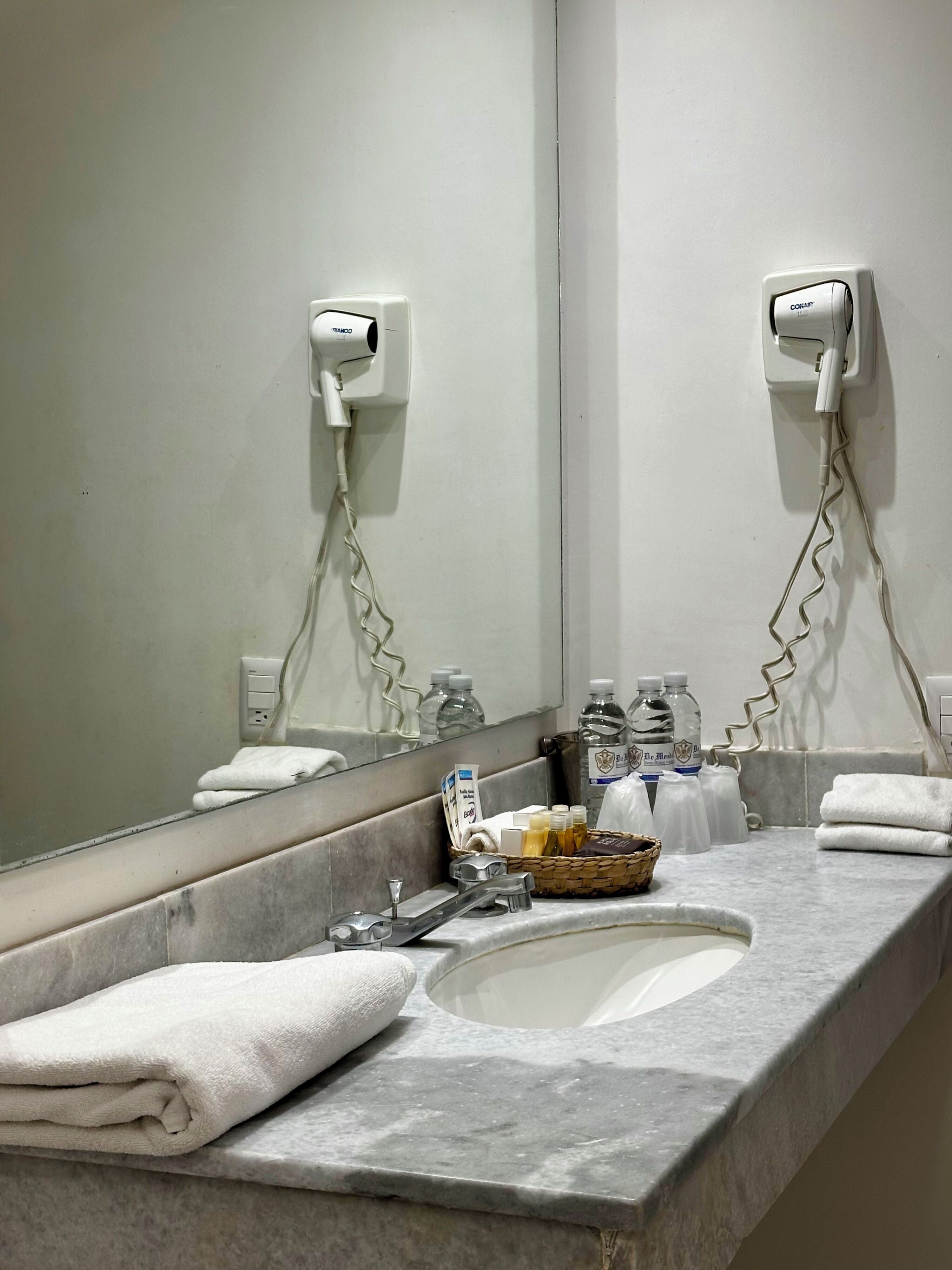 A bathroom with a marble sink, white towels, a hairdryer, and toiletries.