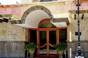 Entrada de hotel con un gran arco, fachada de piedra y dos plantas en macetas.