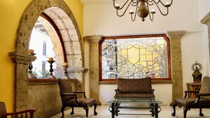 Una habitación con un amplio arco, un ventanal de vitrales y una zona de estar con una mesa de vidrio y sillas estampadas.