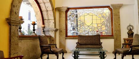 A room with a large arched doorway, a stained glass window, and a seating area with a glass table and patterned chairs.