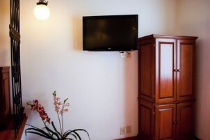 Habitación con televisión de pantalla plana en la pared, un armario de madera y una planta con orquídeas.