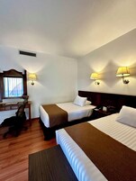 Habitación de hotel con dos camas, un escritorio, una silla y dos lámparas fijadas a la pared.