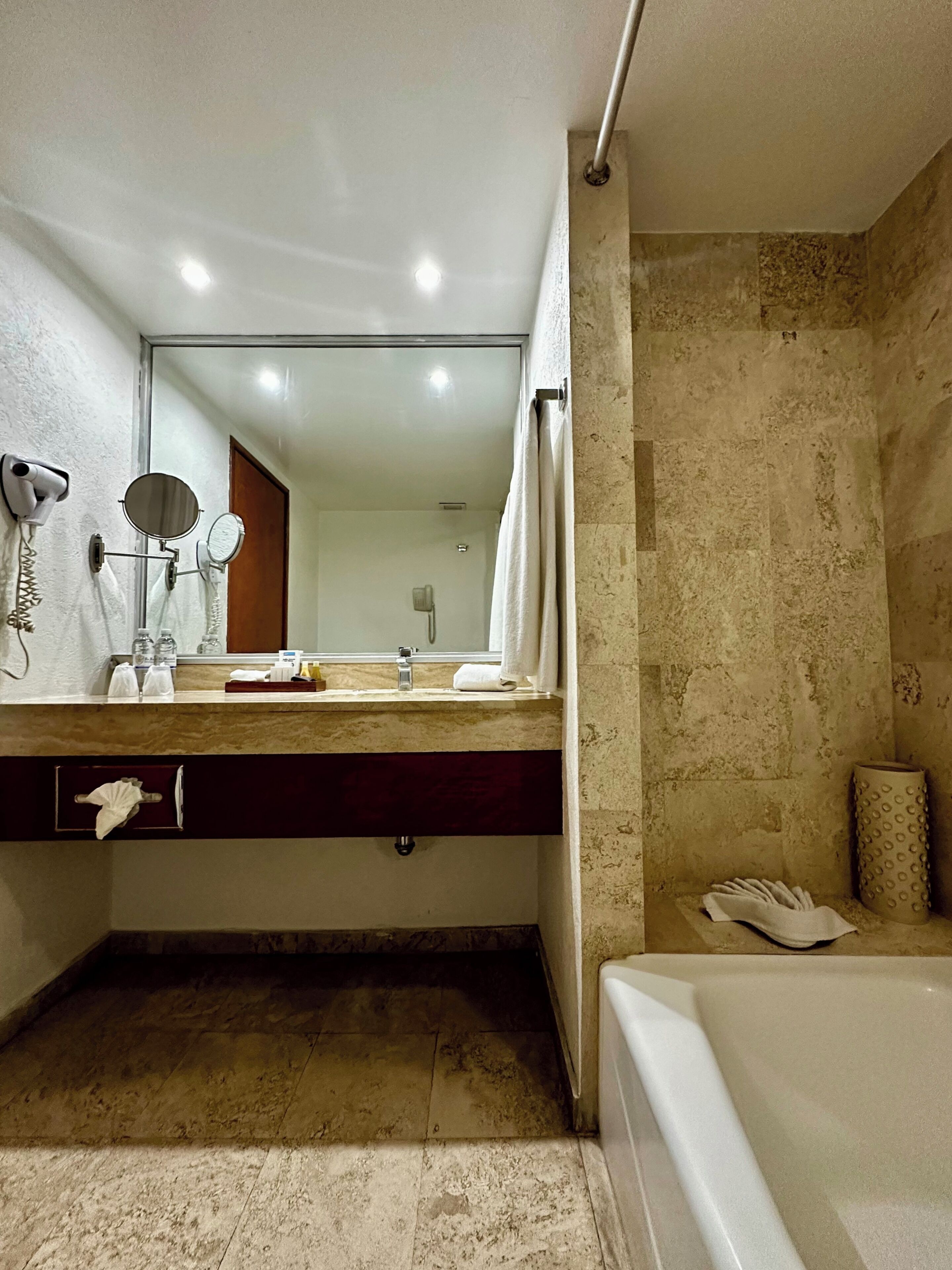 Un baño moderno con un espejo grande, dos secadores de pelo fijos en la pared, un perchero para toallas y una bañera.
