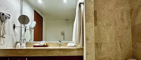 Une salle de bain moderne avec un grand miroir, deux sèche-cheveux fixés au mur, un porte-serviettes et une baignoire.