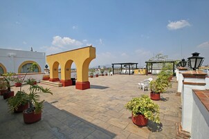 Eine Dachterrasse mit Topfpflanzen, einem gelben Bogen und einem Pavillon.