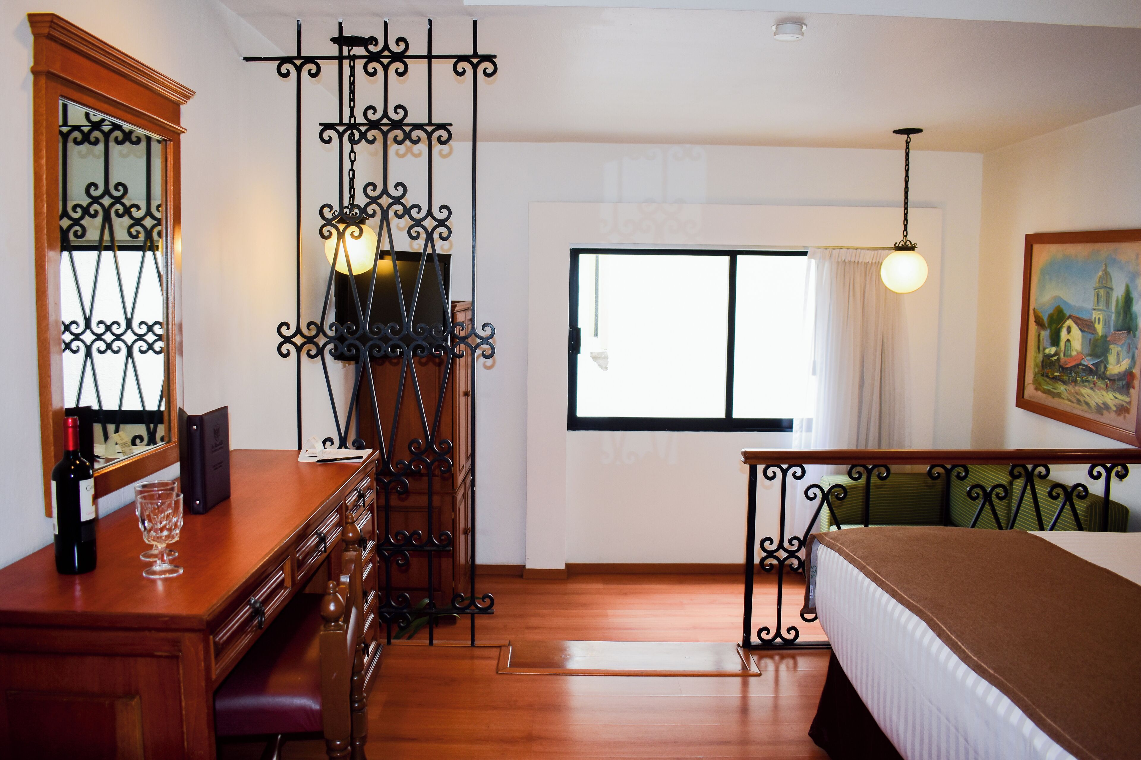 Habitación de hotel con un escritorio de madera, una cama, una ventana con cortinas y un cuadro en la pared.