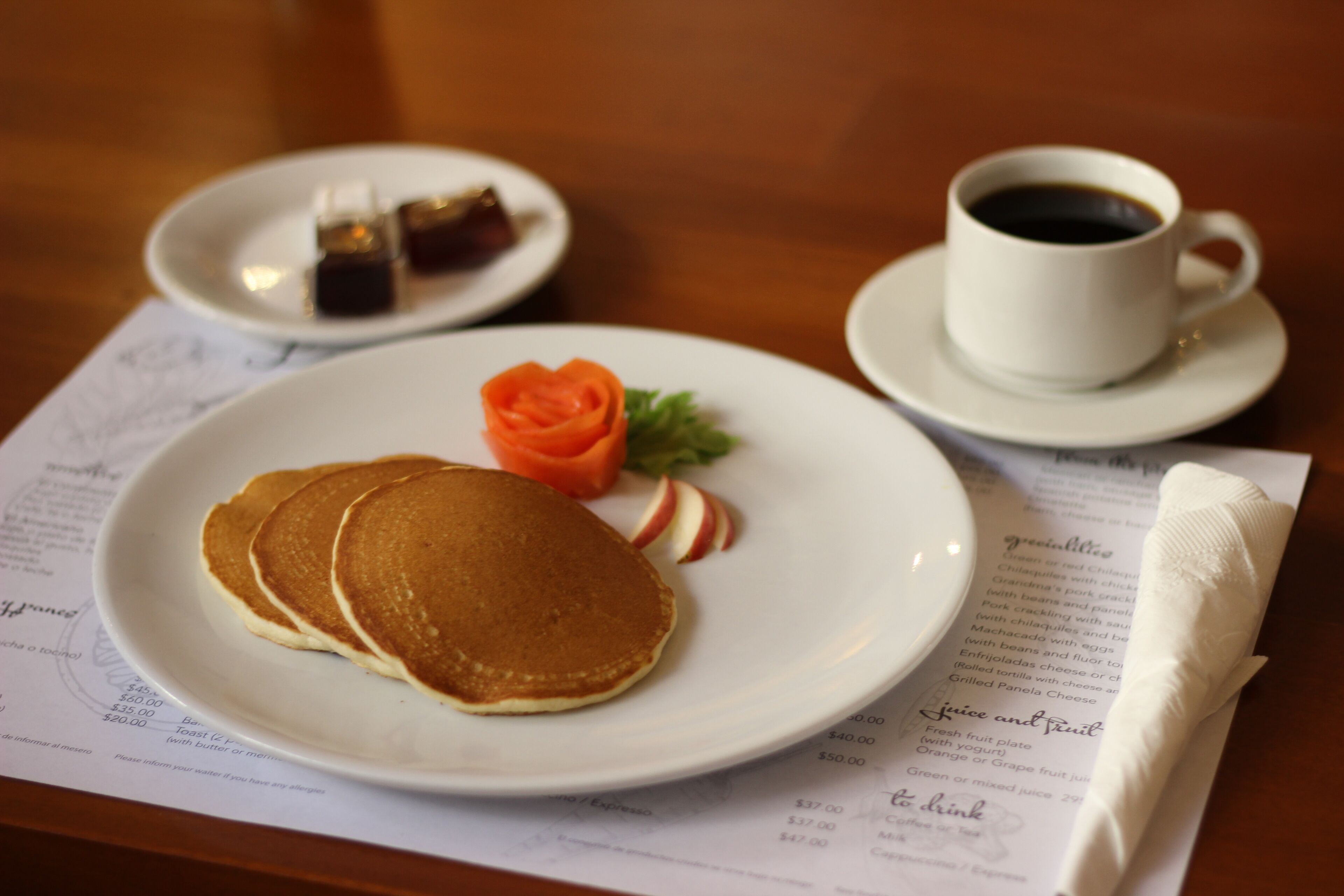 A breakfast setting with pancakes on a plate, a cup of coffee, and a menu.