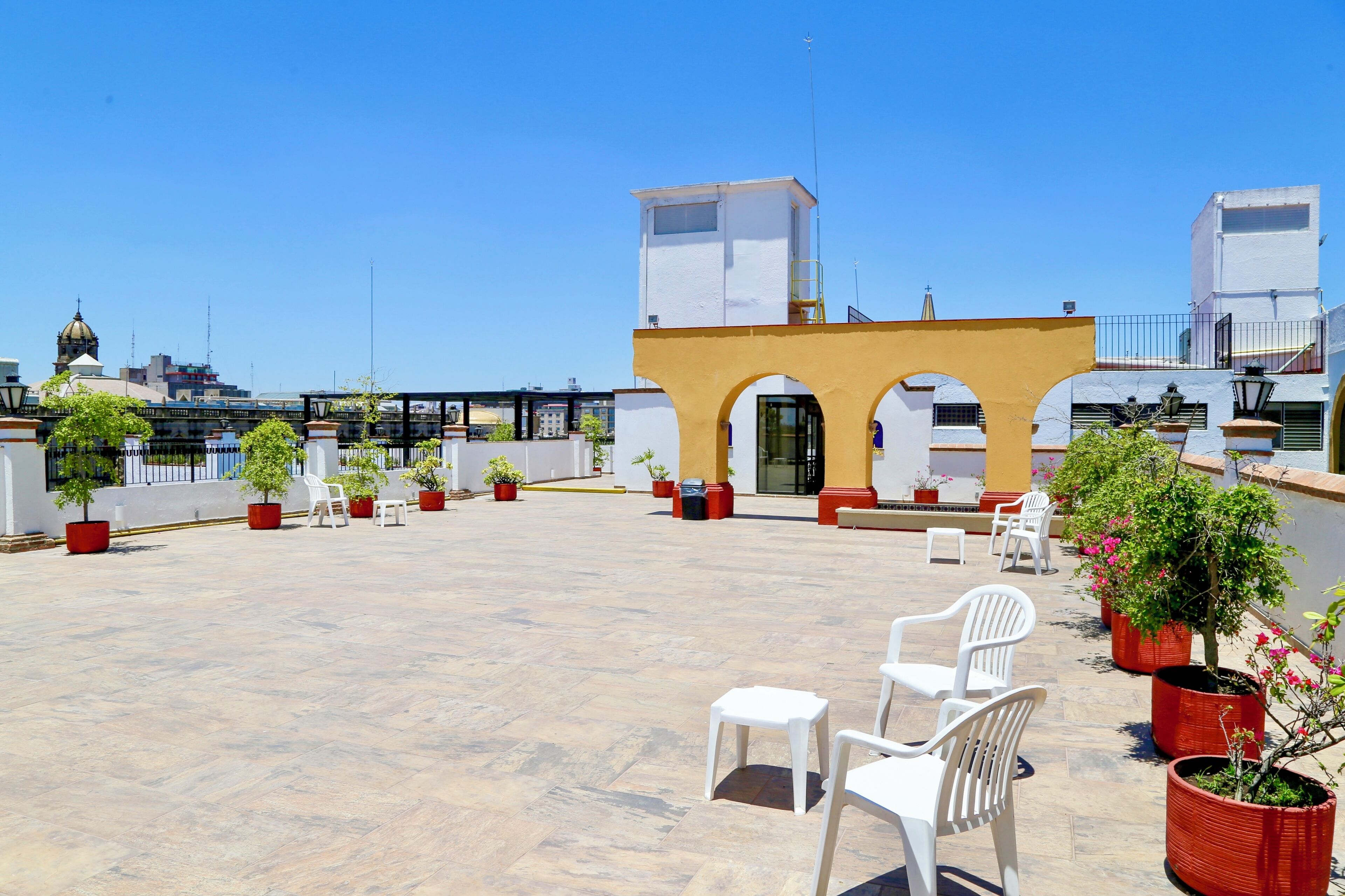 A rooftop terrace with white plastic chairs, potted plants, and a yellow archway.