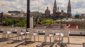 Una terraza con sillas de plástico blancas y vistas a edificios históricos al fondo.