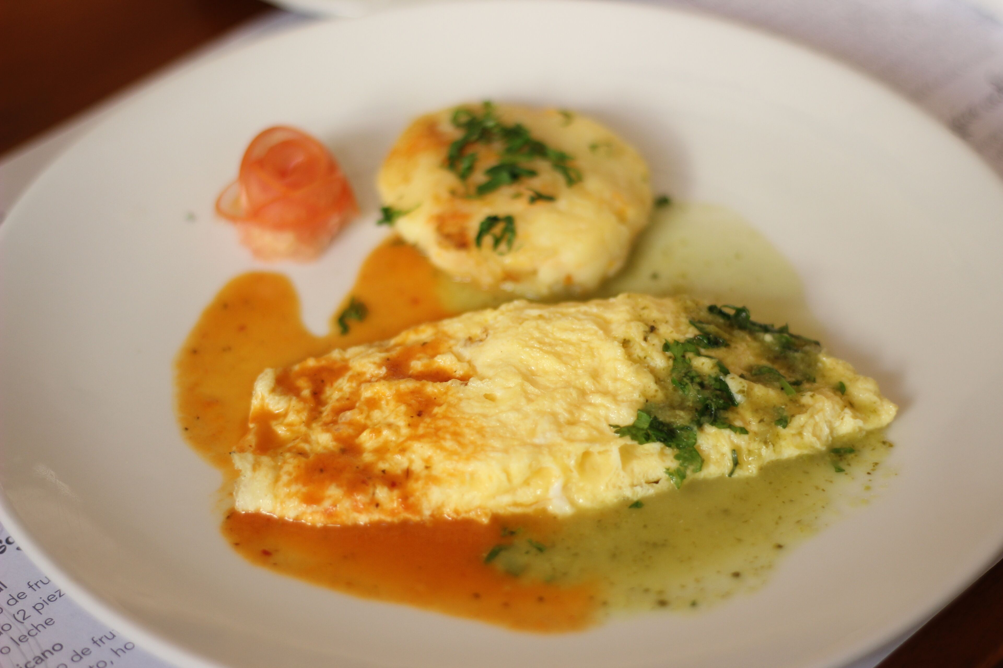 Un plato con huevos revueltos, un trozo de mantequilla y un tomate pequeño.