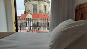 Una habitación de hotel con cama, vista a un edificio histórico y balcón con sillas.