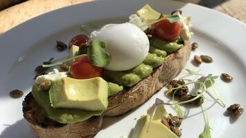 A plate with a sandwich topped with avocado, tomato, and a poached egg, accompanied by a cup of coffee.