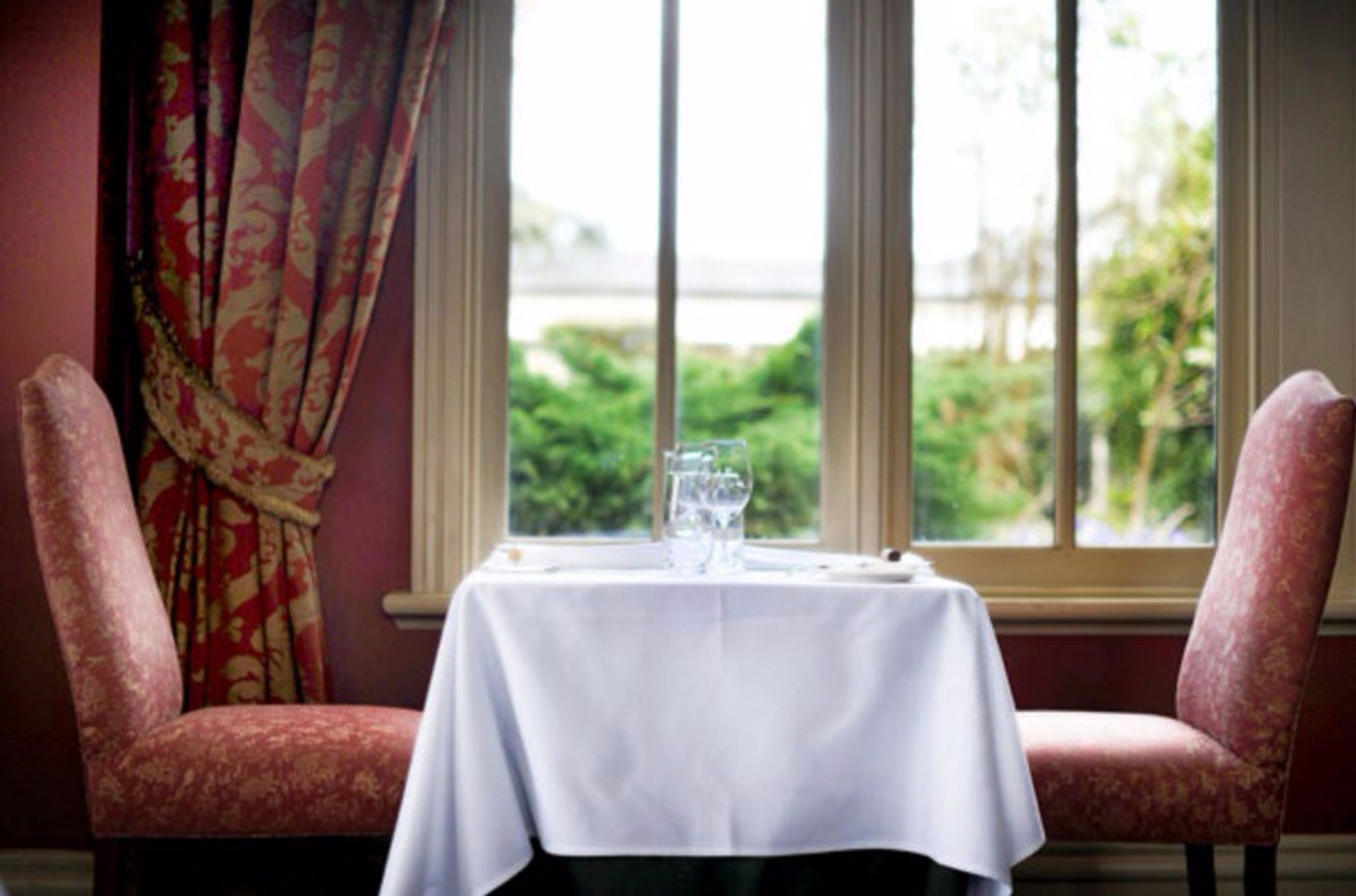 A dining table with a white tablecloth, two red upholstered chairs, and a glass of water on the table.