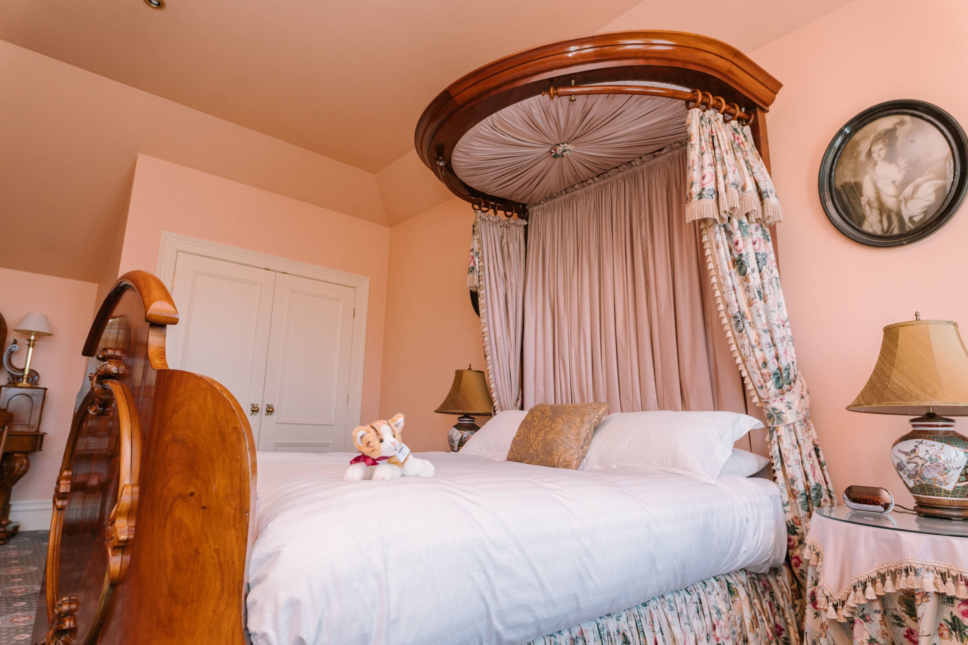 Un dormitorio con cama con dosel, una mesita de noche con lámpara y una cortina estampada con motivos florales.