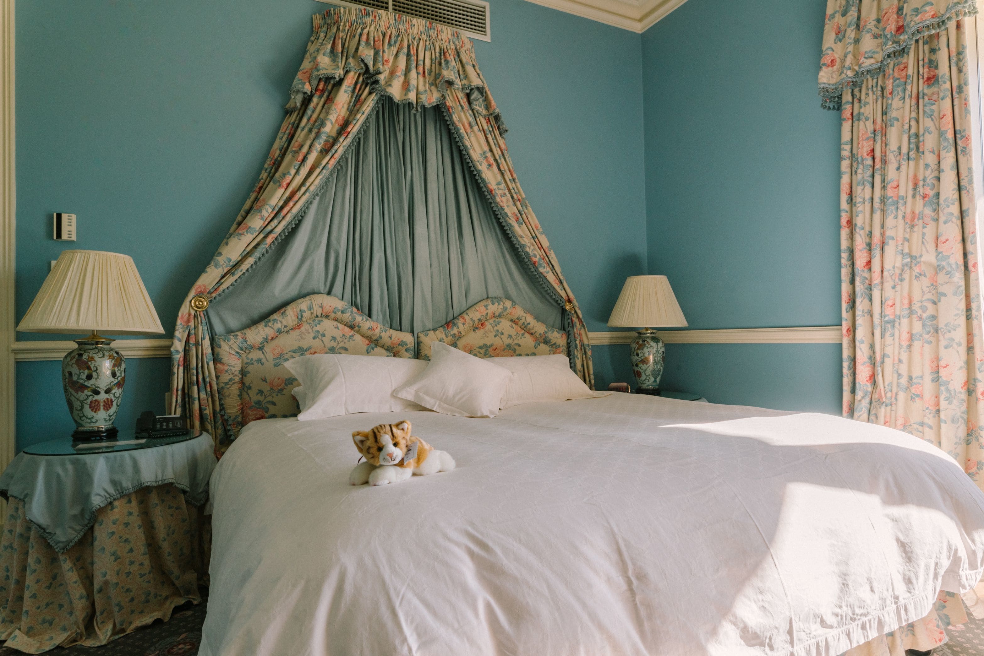 A bedroom with a four-poster bed, floral curtains, and a small table with a lamp.