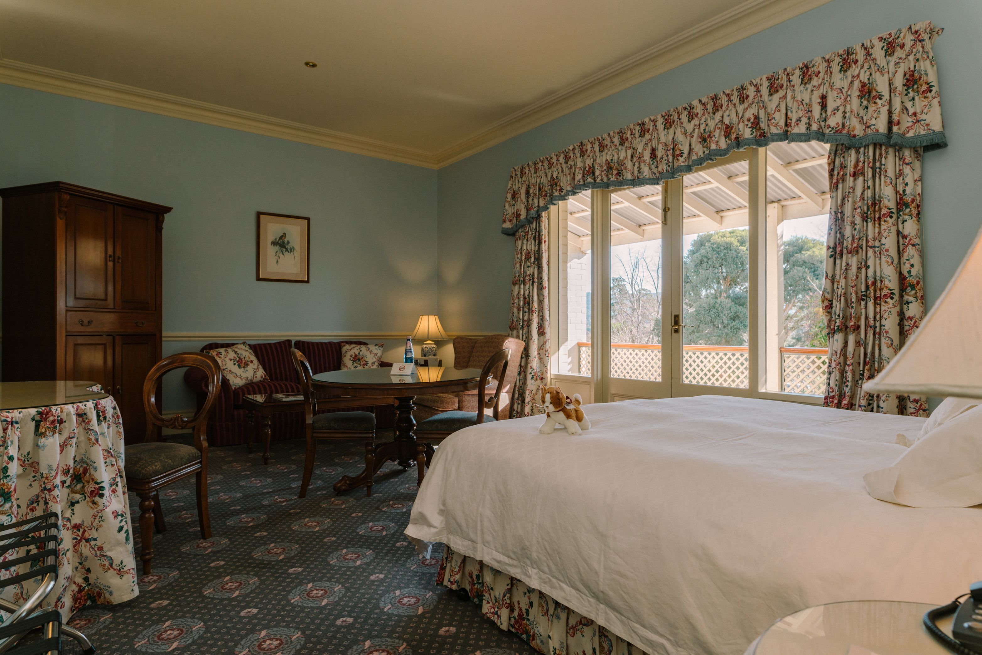 A hotel room with a bed, a desk with a lamp, a chair, a table, and a view of the outdoors.