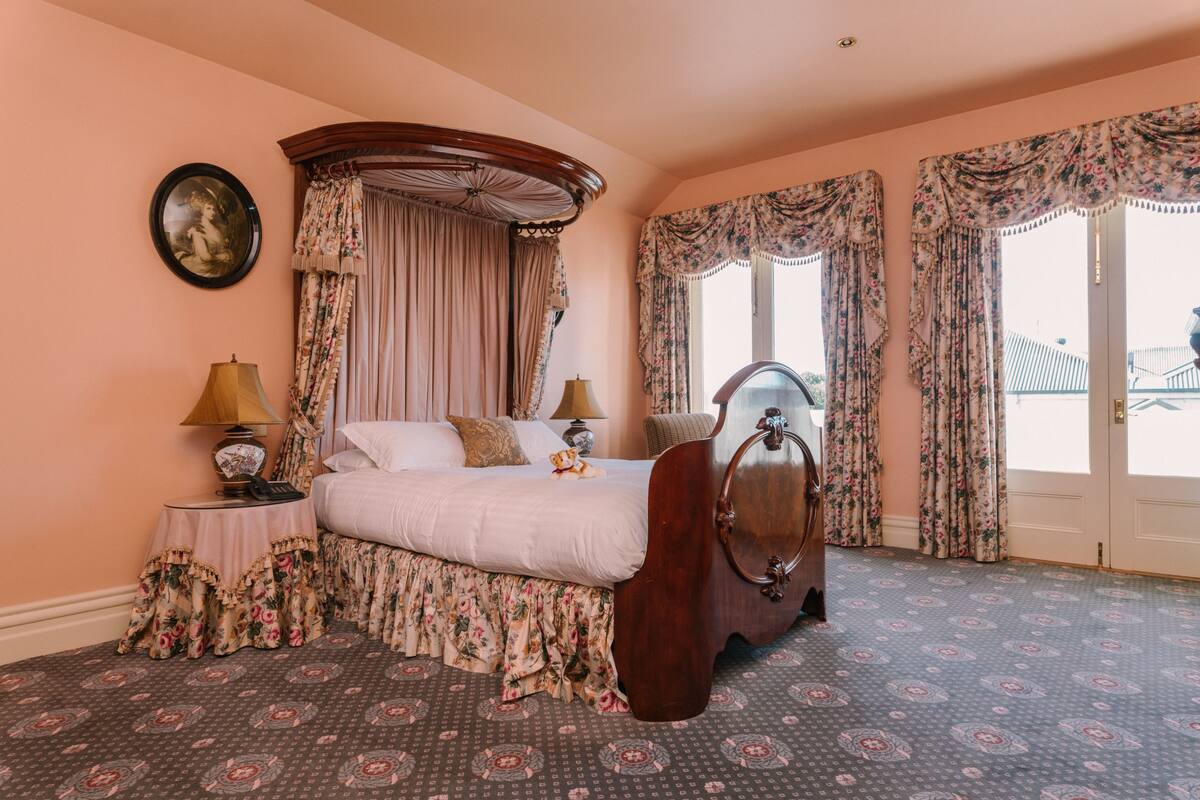A bedroom with a four-poster bed, floral curtains, a round mirror, and a patterned carpet.