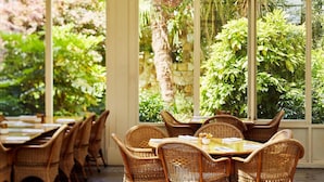 A restaurant with wicker furniture and large windows overlooking a garden. - Chateau Yering Hotel (Yering)