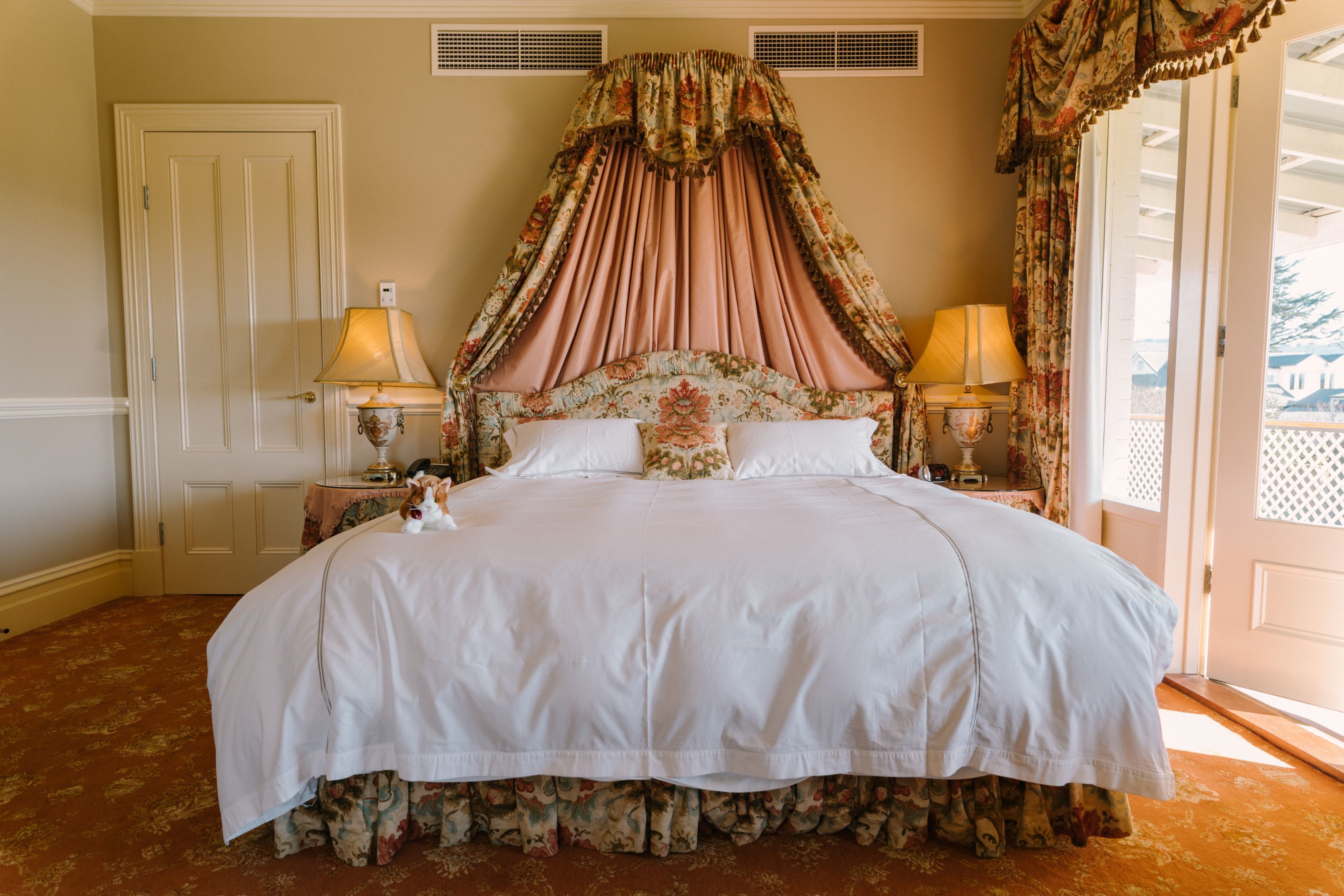 A large bed with a canopy, two bedside lamps, and floral-patterned curtains.