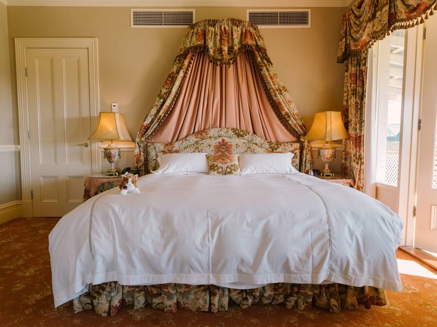 A large bed with a canopy, two bedside lamps, and floral-patterned curtains.
