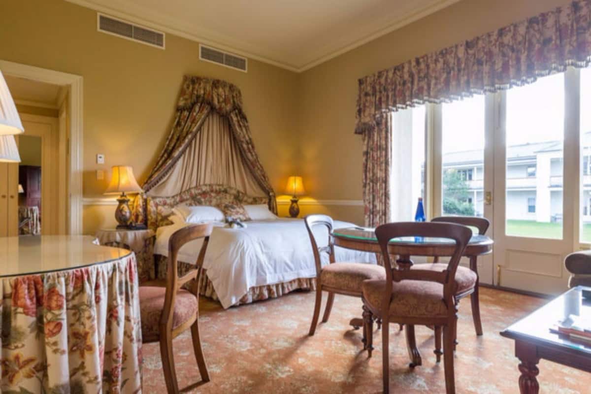 A hotel room with a bed, two chairs, a table, and a window with a view of buildings.