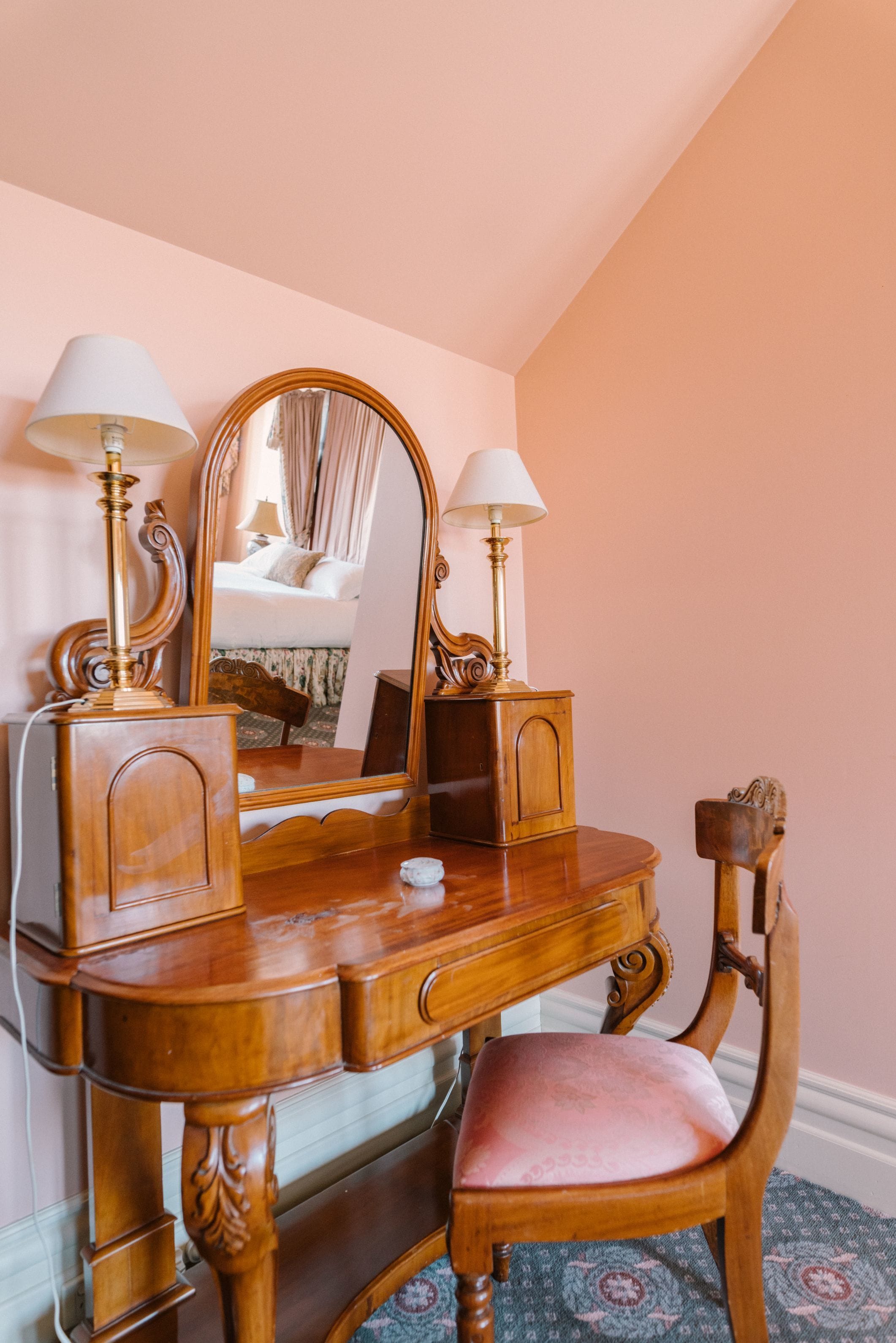 A wooden vanity with a mirror, two lamps, and a chair.