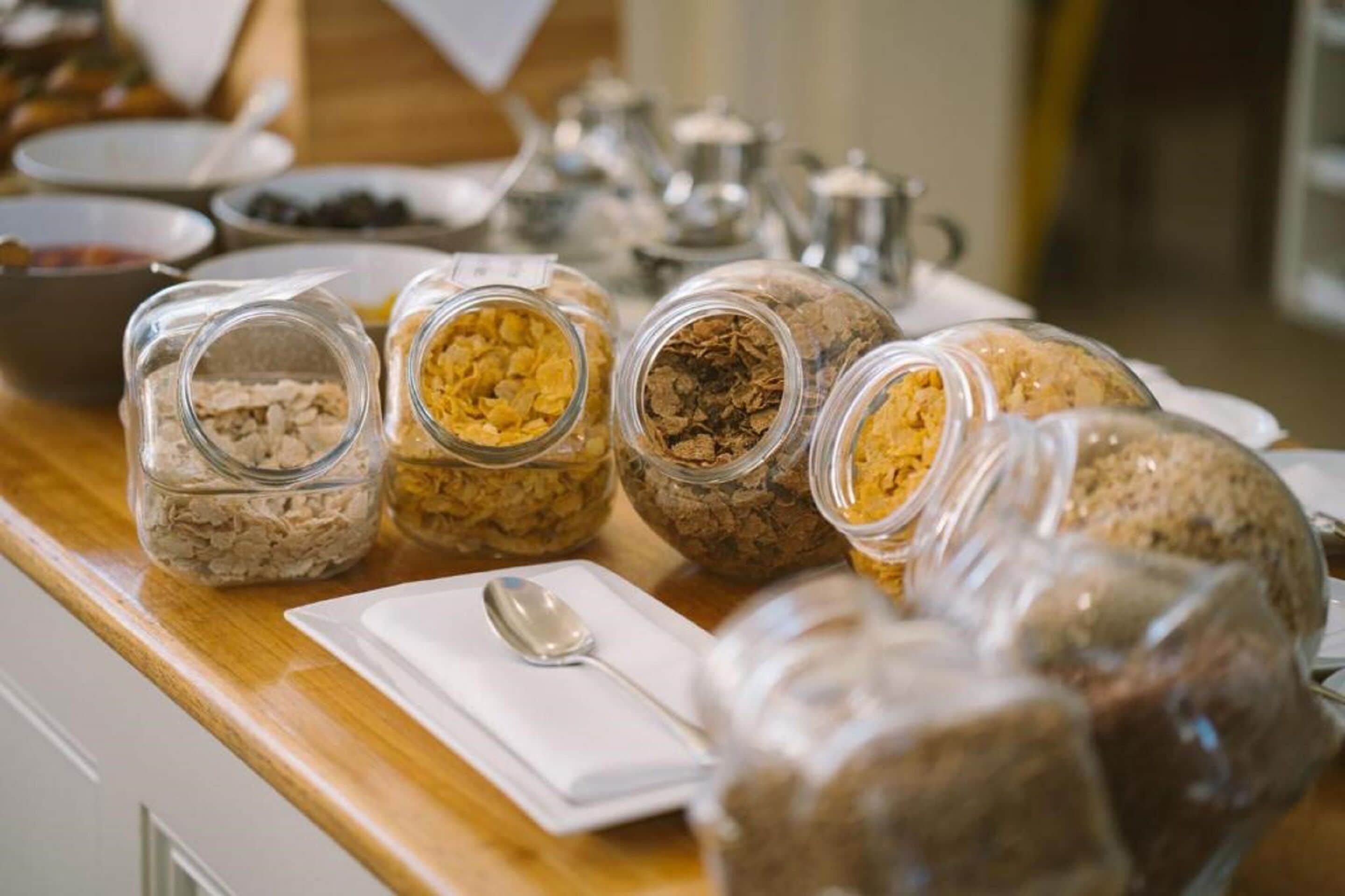Un bufé de desayuno con diversos alimentos en frascos de vidrio sobre una mesa de madera.
